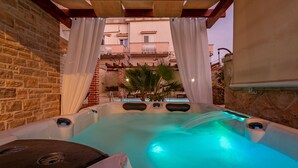 A hot tub with a stone wall backdrop, a brick wall, and a view of a building with balconies. - Villa Ivan ZadarVillas (Novigrad)