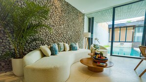 Un salon moderne avec un canapé aux lignes courbes, une table basse ornée de fruits et un mur en pierre.