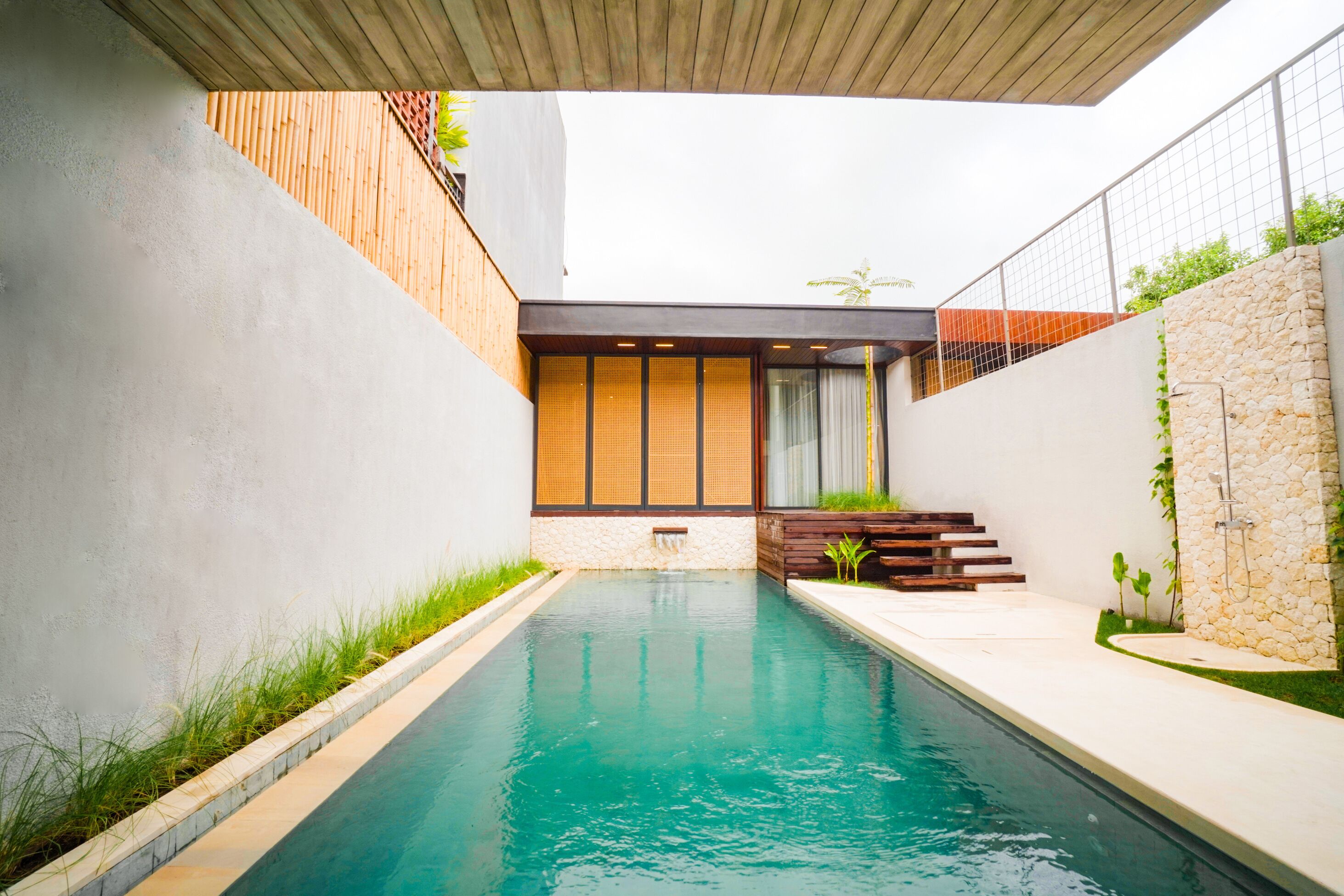 A modern swimming pool with a wooden deck and a stone wall.