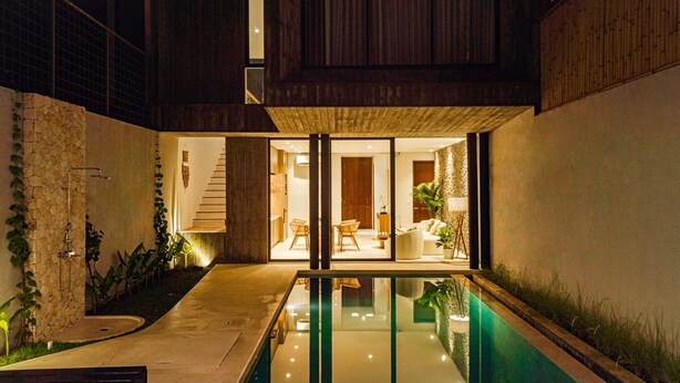 Un espace piscine extérieur moderne, doté d’une paroi en verre, de murs en pierre et d’une terrasse en bois.
