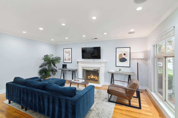 A modern living room with a blue sectional sofa, a fireplace, a television, and a large window.