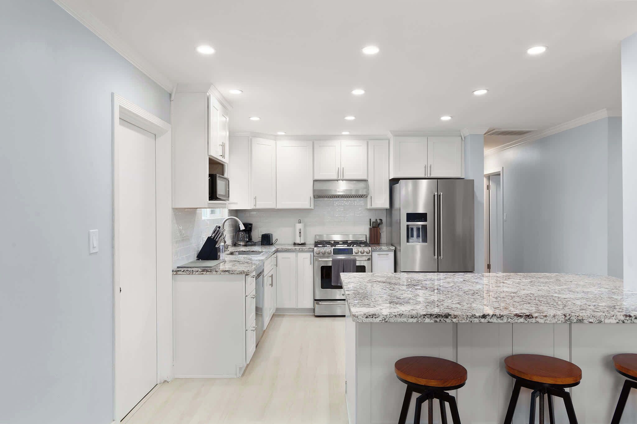 A modern kitchen with white cabinets, stainless steel appliances, and a marble countertop.