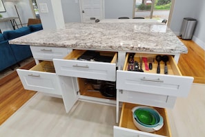 A kitchen with a granite countertop, white cabinetry, and a built-in drawer with utensils.