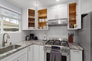 A modern kitchen with white cabinets, a granite countertop, a stainless steel stove, and a window with blinds. - @ Marbella Lane - Immaculate & Cozy 3BR Home (San Jose)