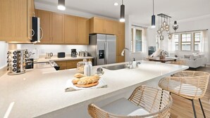 Eine moderne Küche mit Holzschränken, einem Edelstahlkühlschrank und einer großen Kochinsel mit Sitzgelegenheiten.