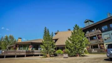 A building with a sloped roof, large windows, and a balcony. There are trees in front of the building.