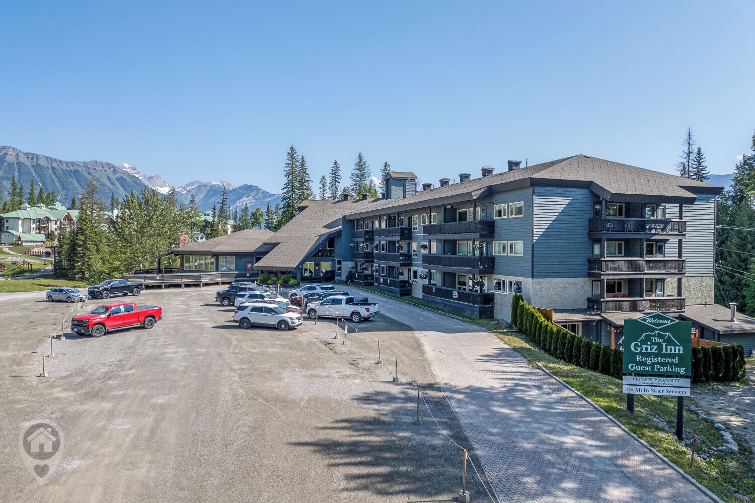 Un immeuble à plusieurs étages avec un parking devant, une enseigne indiquant « The Griz Inn », et des montagnes en arrière-plan.