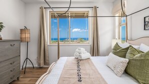 Ein Schlafzimmer mit Bett, einem Fenster mit Vorhängen, einer Nachttischlampe und Meerblick.