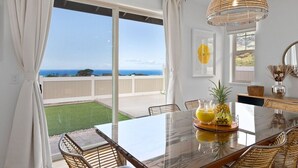 Ein Essbereich mit einem großen Tisch, Stühlen und Blick auf das Meer.