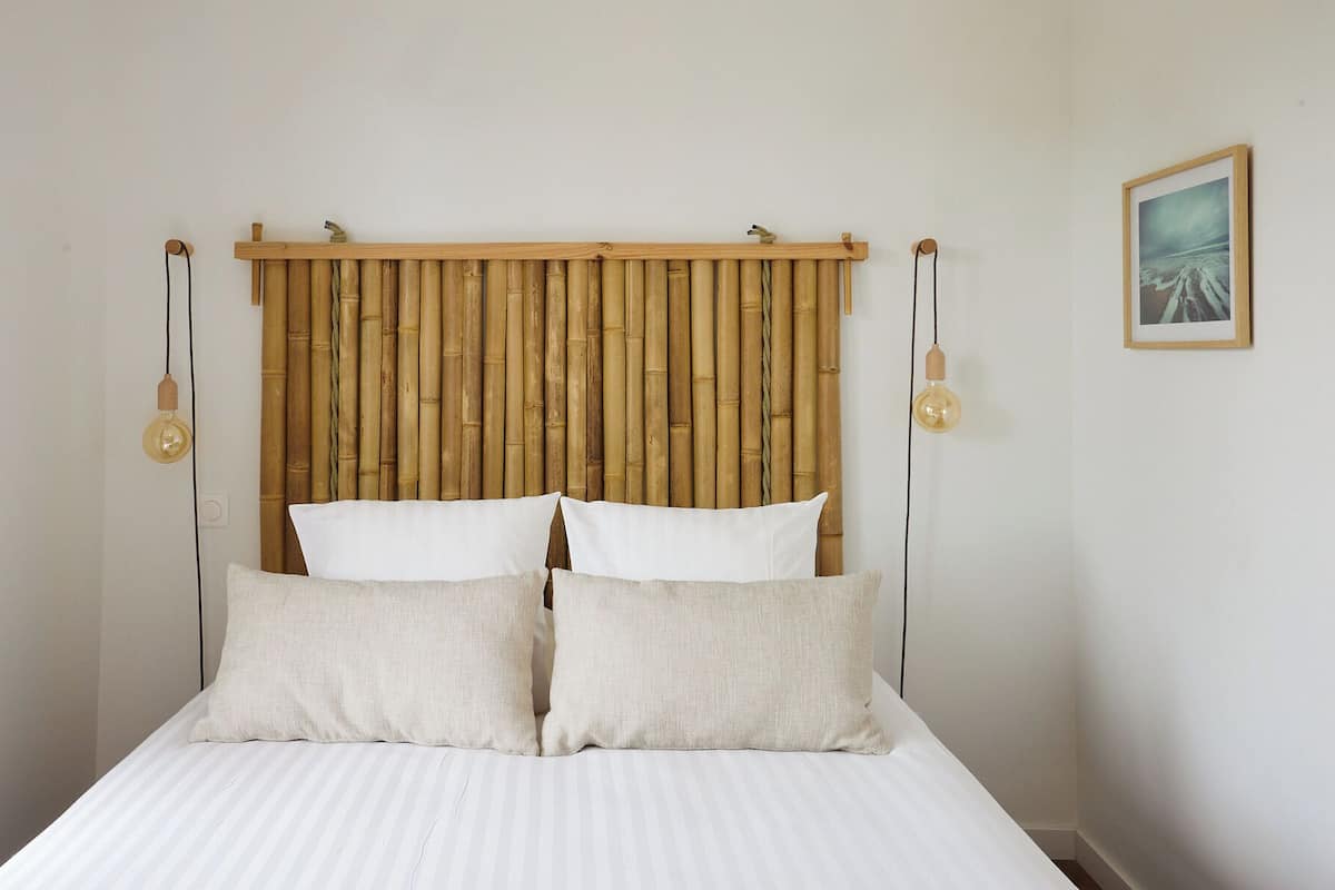 A bed with a bamboo headboard, two pillows, and two wall-mounted light fixtures.
