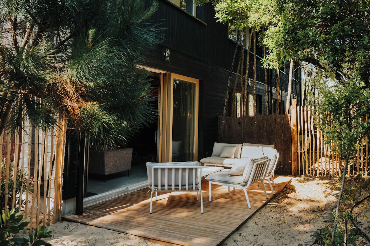 An outdoor patio with a wooden deck, white furniture, and a glass door leading to a covered area.
