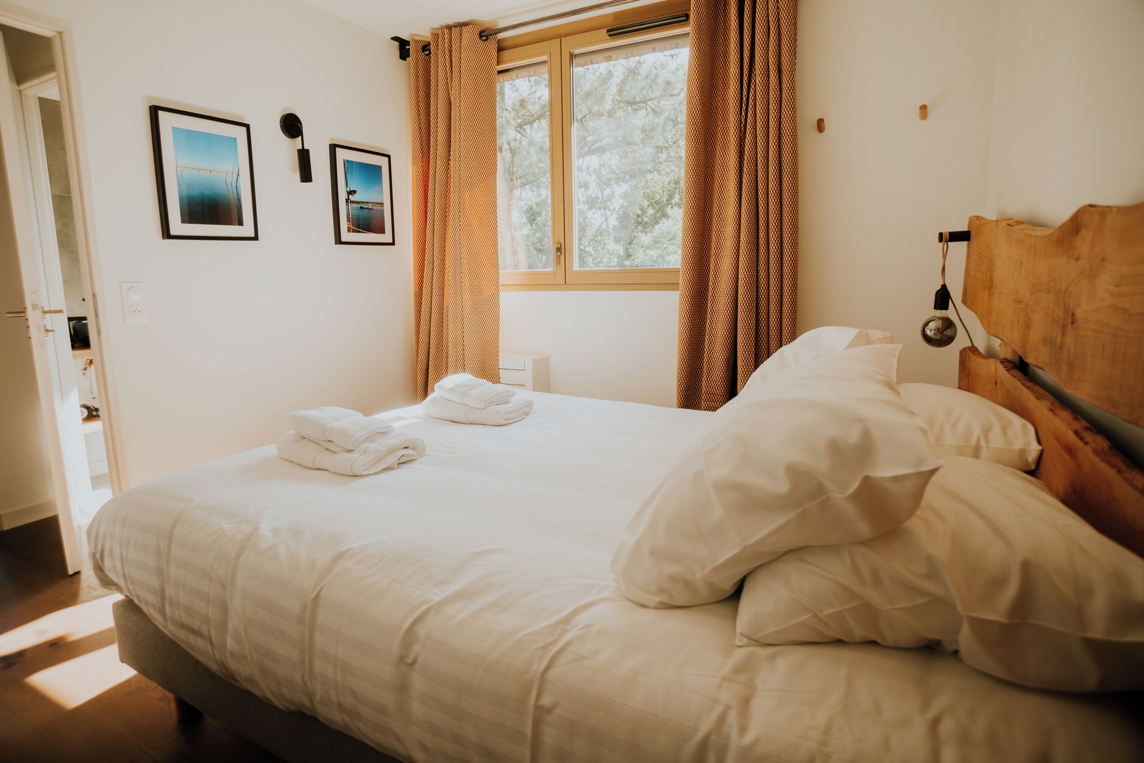 A neatly made bed with white linens, a wooden headboard, and two framed pictures on the wall.