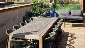 An outdoor dining area with a wooden table and chairs, a cushioned seating area, and a pool in the background. - Kaze Océan The Originals Relais (Lège-Cap-Ferret)