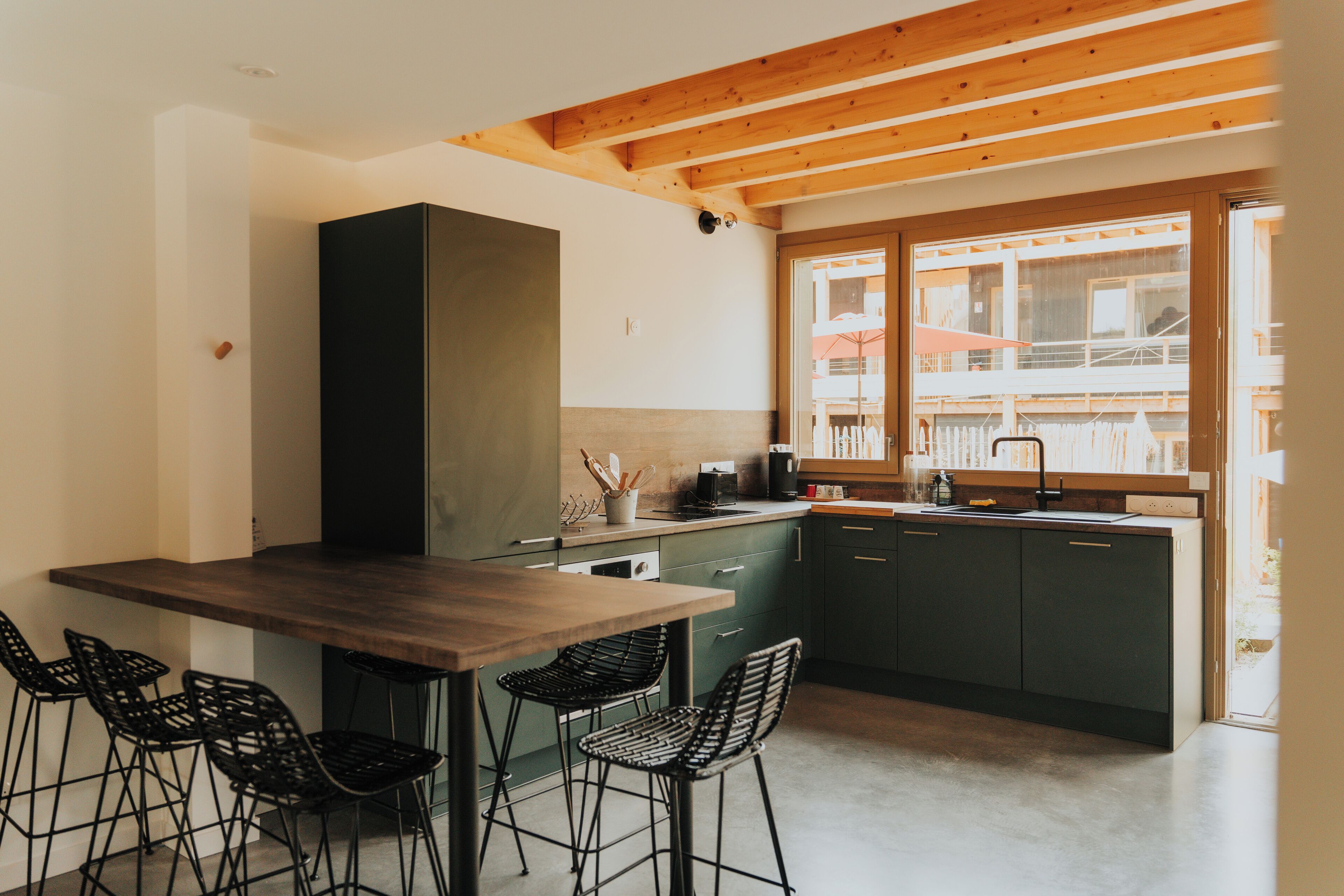 A modern kitchen with a wooden ceiling, dark cabinets, and a large window.