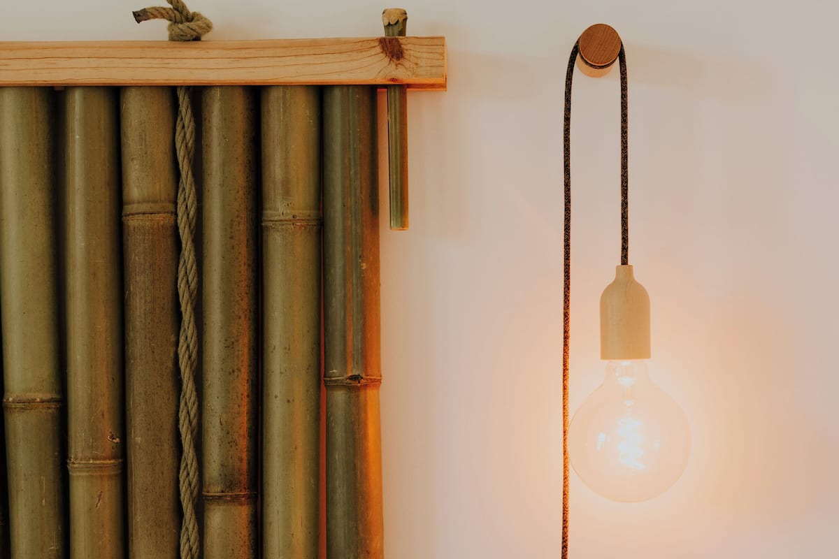 A bed with white bedding, a bamboo curtain, and a hanging light fixture.