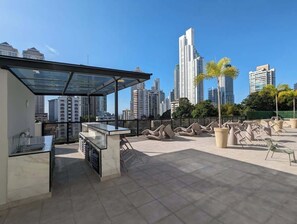 Een terras op het dak met glazen wanden, buitenmeubels en uitzicht op een stadshemelbeeld.