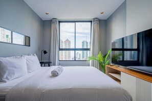 Habitación de hotel con cama, televisor, escritorio, lámpara y ventana con vista a la ciudad.