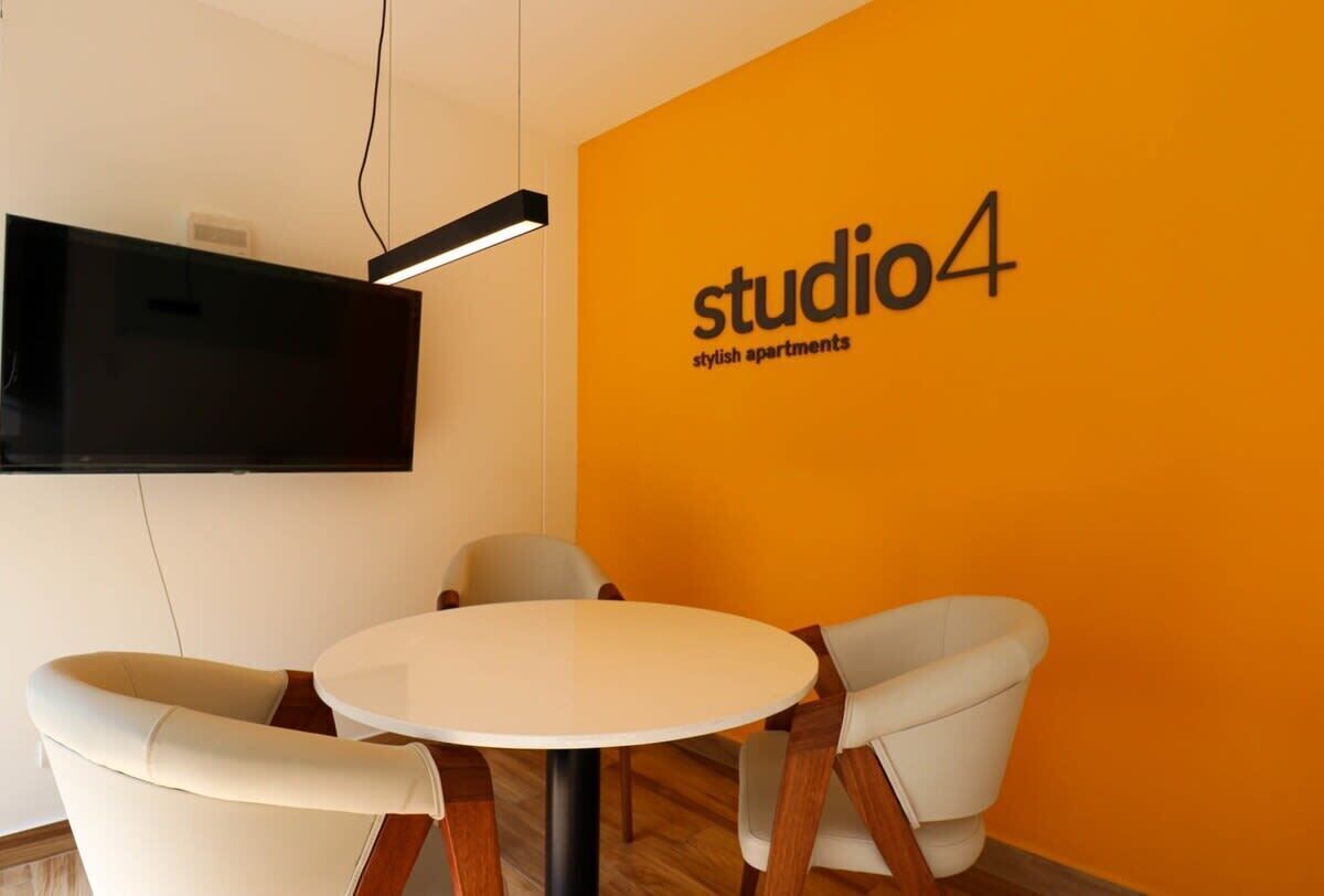 A modern interior with a round table and two chairs, a mounted TV, and a wall with 'studio4 stylish apartments' text.