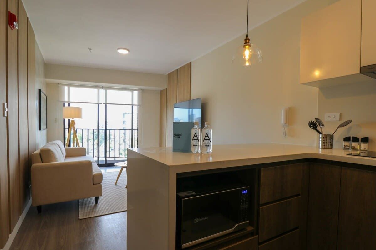 A modern kitchen with a built-in microwave, a dining area with a sofa, and a large window offering a view of the outdoors.
