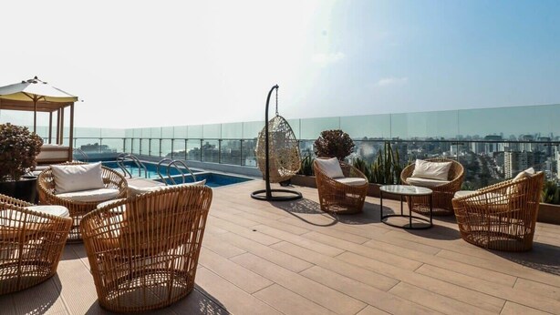 Una terraza en la azotea con mobiliario de mimbre, una silla colgante y vistas del horizonte de la ciudad.