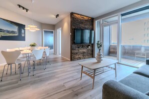 A modern living room with a dining area, a stone fireplace, and a large TV.
