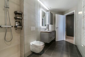 A modern bathroom with a glass-enclosed shower, a white toilet, and a vanity with a mirror. - SIF Apartments - 2 bedrooms with 2 bathrooms (Reykjavík)