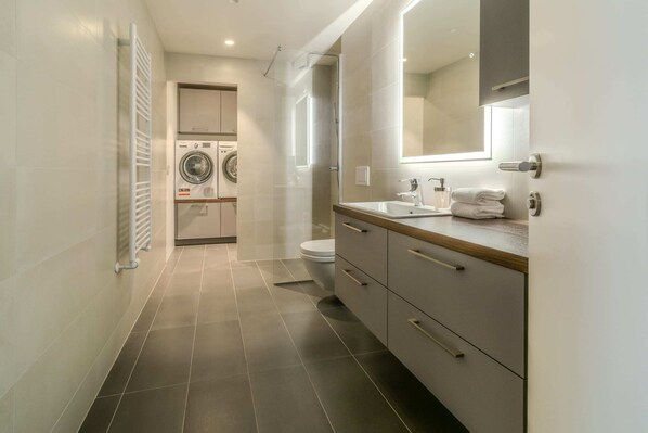 A modern bathroom with a built-in washing machine, a toilet, and a vanity with a mirror.