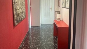 A hallway with a red wall, a black speckled floor, a white door, and a small table with a lamp. - Panoramic two-room apartment on the banks of the Dora River - Da Momo (Torino)