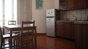 A kitchen with wooden cabinets, a white refrigerator, and a dining table with chairs. - Panoramic two-room apartment on the banks of the Dora River - Da Momo (Torino)