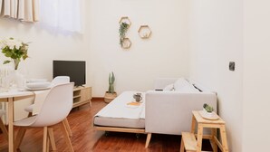 Una sala de estar minimalista con un sofá, una mesita, un televisor y una planta en maceta.