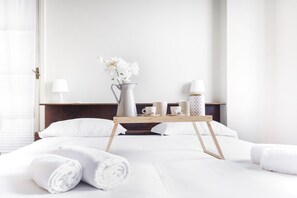 A hotel room with a bed, white towels, a bedside table with a vase of flowers, and a tray with cups and a water bottle. - Easylife - Class and charm in the city center (Milano)