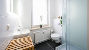 Un bagno moderno con lavandino, water e zona doccia, tutto in bianco.