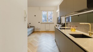 A modern kitchen with a built-in oven, a sink with a gold faucet, and a window with a view of buildings. - Easylife - Charming nest in Sant'Ambrogio (Milano)