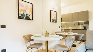A modern dining area with a round table, six chairs, and a kitchen in the background. - Easylife - Charming nest in Sant'Ambrogio (Milano)