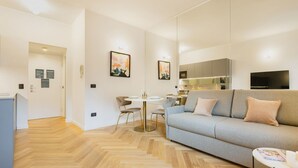 A modern living room with a sofa, a dining table, and chairs. There is a kitchen area with cabinets and a TV. - Easylife - Charming nest in Sant'Ambrogio (Milano)