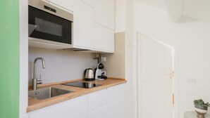 Uma cozinha compacta com micro-ondas, pia de aço inoxidável e cafeteira em bancada de madeira.
