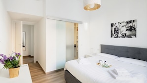 Une chambre d’hôtel moderne avec un grand lit, une table de chevet avec une lampe, un tableau accroché au mur et une plante en pot.