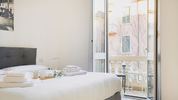 Une chambre d’hôtel avec un lit, une petite table sur laquelle se trouvent des serviettes et une tasse, et une vue sur un balcon agrémenté de chaises et d’une balustrade.