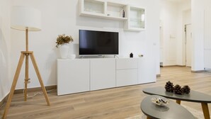 Un salon moderne avec un téléviseur à écran plat posé sur un meuble blanc, un lampadaire et une petite table agrémentée d’objets décoratifs.