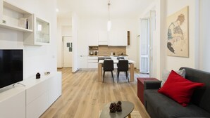 Un salon moderne doté d’un téléviseur à écran plat, d’un coussin rouge et d’un coin repas avec une table et des chaises en bois.