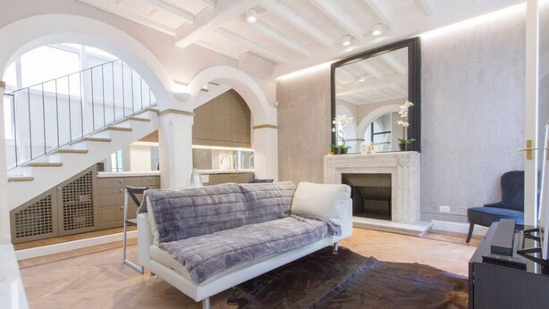 A modern living room with a sofa, a fireplace, a staircase, and a large mirror.