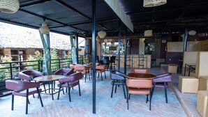 An outdoor seating area with tables and chairs, a bar in the background, and a view of a mountain. - The Country Inn by Smart Haven (Kigali)