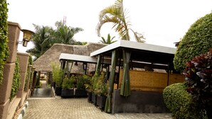A paved courtyard with a thatched-roof structure, potted plants, and a covered seating area. - The Country Inn by Smart Haven (Kigali)