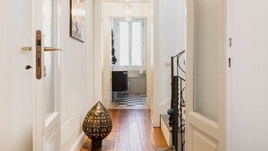 A hallway with a wooden floor, a decorative lamp, and a staircase with a black railing.