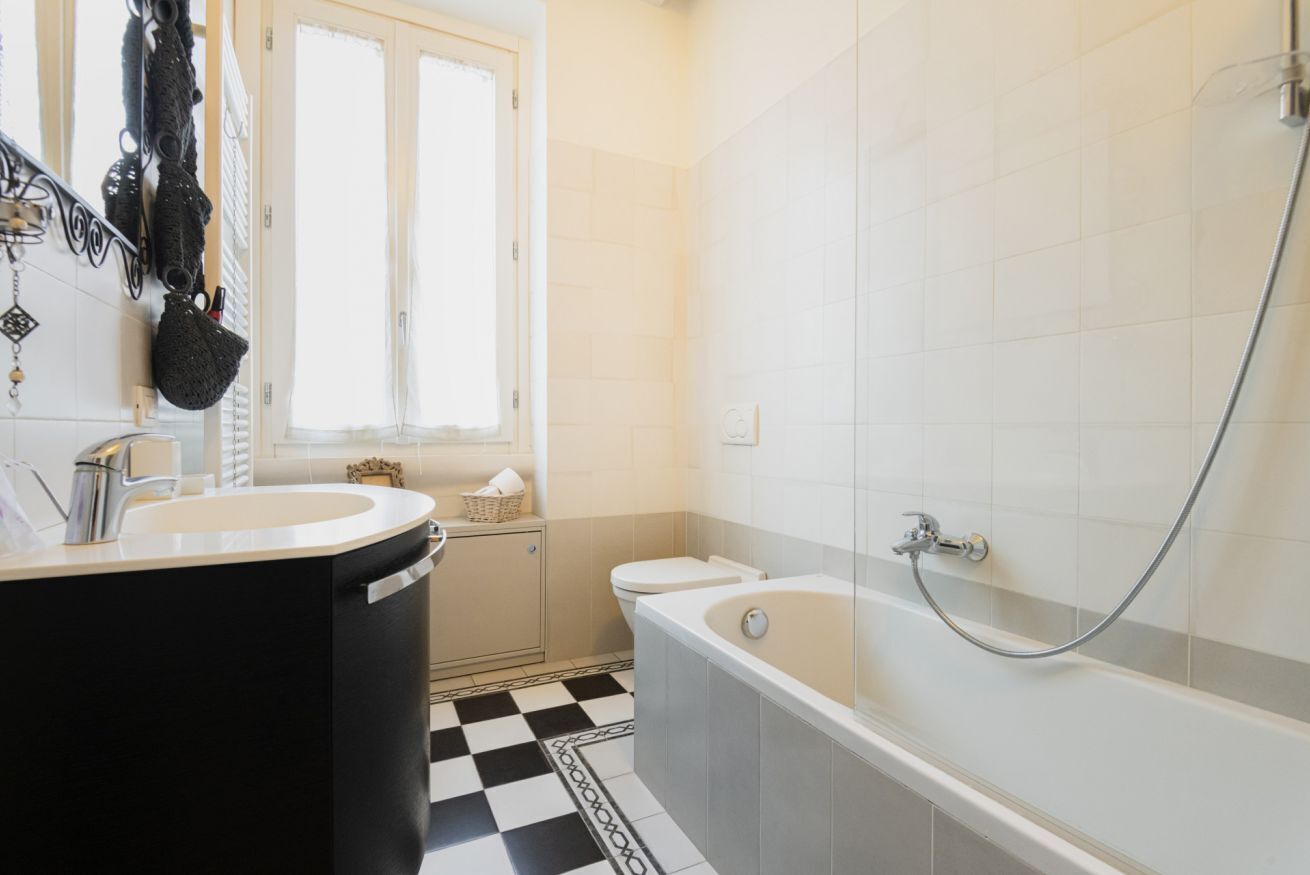 Une salle de bain avec un carrelage noir et blanc à motifs géométriques, une baignoire blanche et un lavabo avec un miroir.