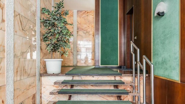 A marble staircase with green carpeted steps and metal railings, leading to a wooden door with a green panel.
