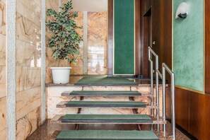 Eine Marmortreppe mit grünem Teppich und Metallgeländern, die zu einer Holztür mit einem grünen Feld führt.