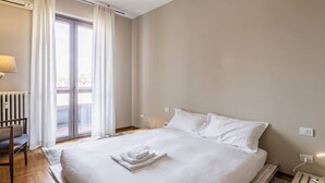 A hotel room with a large bed, a chair, a desk, and a view of the outside through a sliding door.