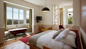 Un dormitorio con una cama grande, una bañera antigua y un televisor en la pared.