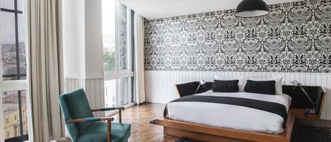 A modern bedroom with a large bed, a teal armchair, and a patterned wallpaper.